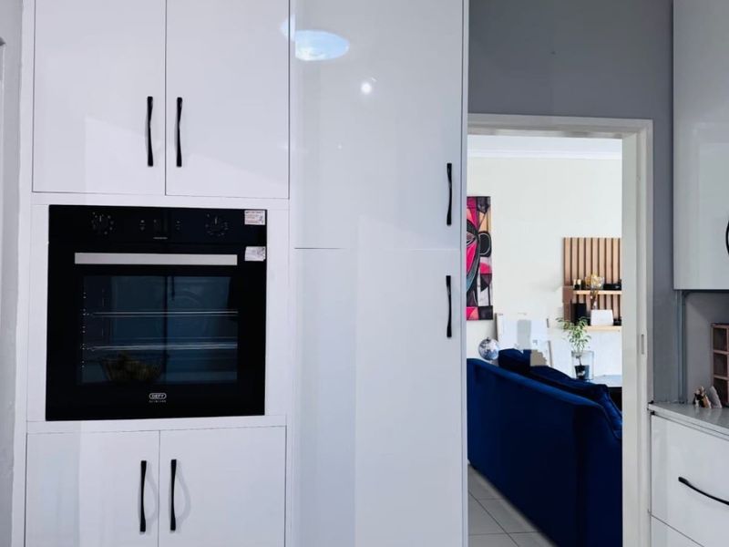 Modern kitchen featuring high-gloss white cabinetry and a built-in oven, with a seamless transition into the adjacent living area.