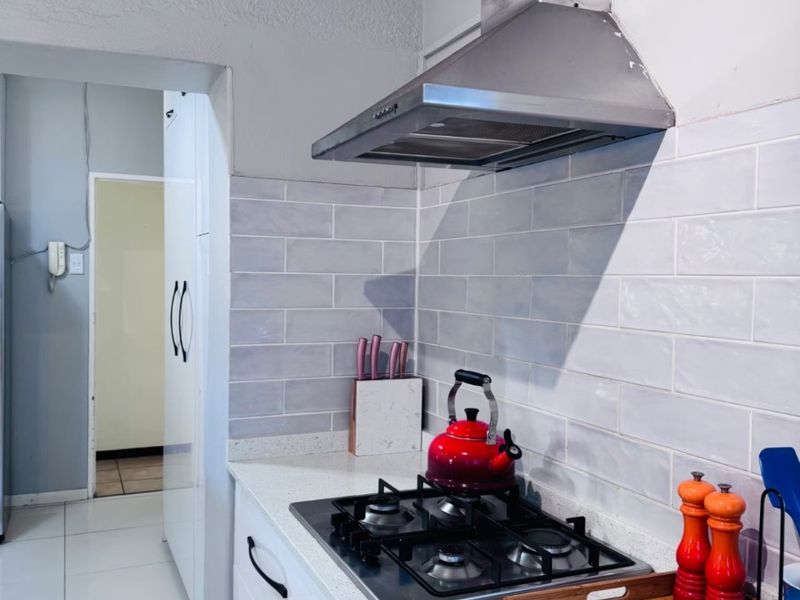 Modern kitchen featuring a gas hob, stainless steel extractor fan, quartz countertops, and stylish subway tile backsplash with ample built-in cabinetry.