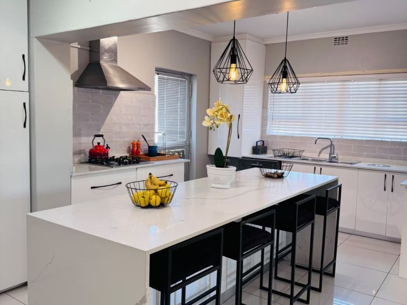 Modern kitchen featuring a large quartz island, gas hob, stainless steel extractor, subway tile backsplash, and sleek white cabinetry with polished floor tiles.