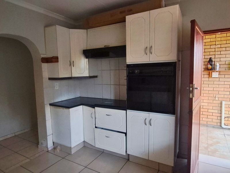 A functional kitchen featuring built-in cabinetry, a tiled backsplash, and a built-in oven, with an adjacent doorway leading to an outdoor area.