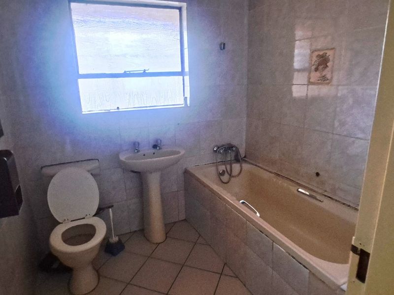 A dated bathroom featuring a pedestal basin, bathtub, and tiled finishes, offering a blank canvas for a modern renovation.