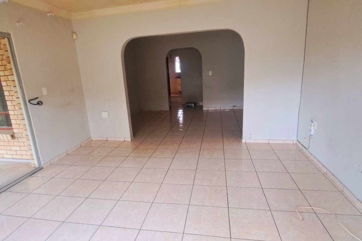 An empty living room featuring tiled flooring, an arched transition to the adjacent space, and a large sliding glass door leading to the exterior.