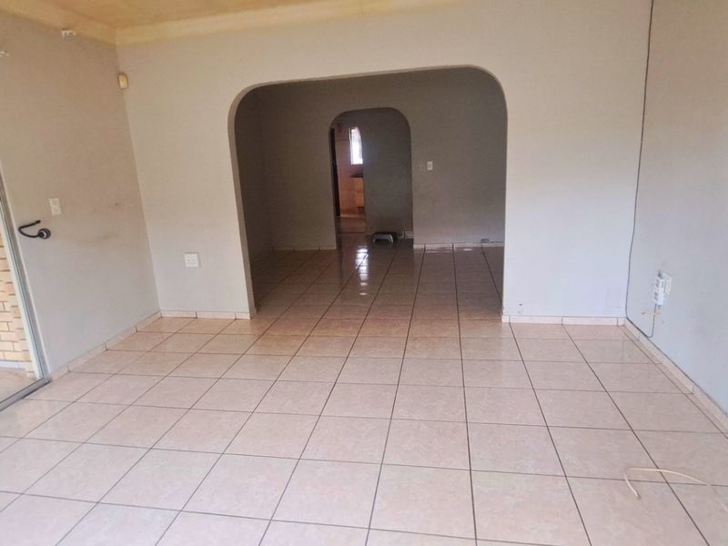 An empty living room featuring tiled flooring, an arched transition to the adjacent space, and a large sliding glass door leading to the exterior.