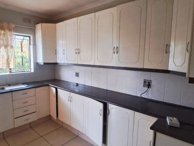 A functional kitchen featuring white cabinetry, laminate countertops, and a double basin sink, offering a practical layout with potential for modern updates.