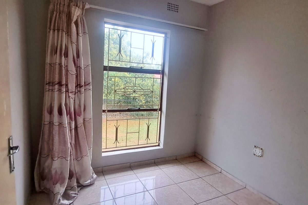 An empty bedroom featuring tiled flooring, a window with security bars, and a curtain rail, ready for personalization.
