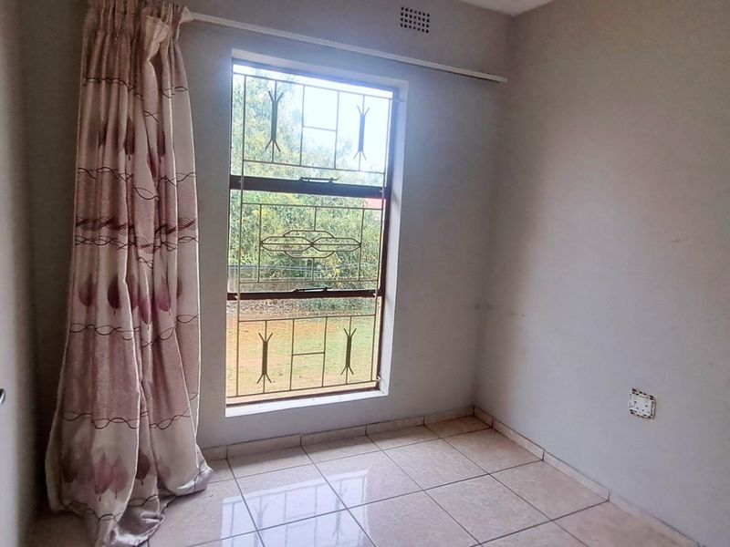 An empty bedroom featuring tiled flooring, a window with security bars, and a curtain rail, ready for personalization.