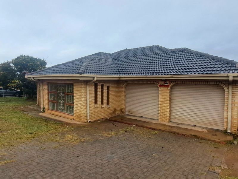 Front view of a single-story brick house featuring a double garage with roller shutter doors and a paved driveway.