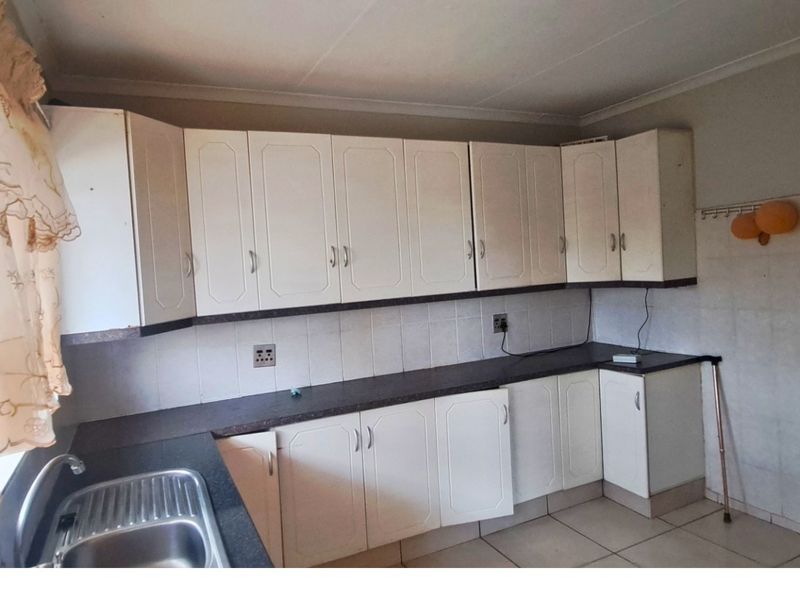 A dated kitchen featuring white built-in cabinetry, laminate countertops, and a stainless steel sink, offering a functional layout ready for modern updates.