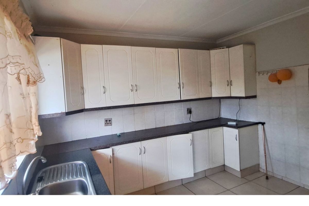 A dated kitchen featuring white built-in cabinetry, laminate countertops, and a stainless steel sink, offering a functional layout ready for modern updates.