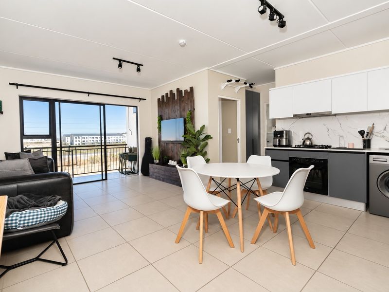 Modern open-plan living area featuring a sleek kitchen with built-in appliances, tiled flooring, and large sliding doors leading to a balcony.
