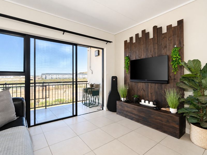 Modern living room featuring tiled floors, a custom wooden feature wall, and large sliding doors opening onto a private balcony with scenic views.