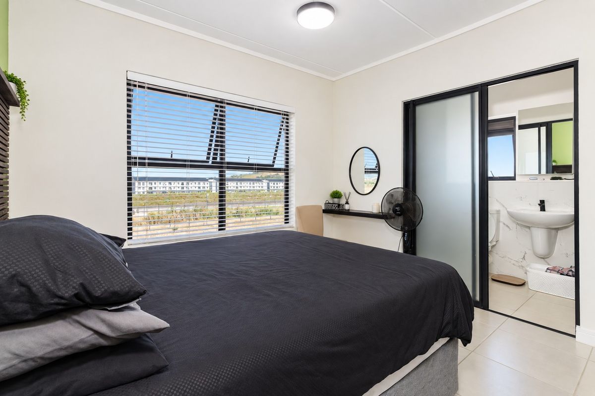 A well-maintained bedroom featuring tiled flooring, aluminium window frames with blinds, and an integrated en-suite bathroom with a sliding glass door.