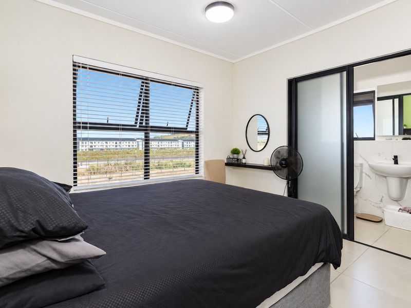 A well-maintained bedroom featuring tiled flooring, aluminium window frames with blinds, and an integrated en-suite bathroom with a sliding glass door.