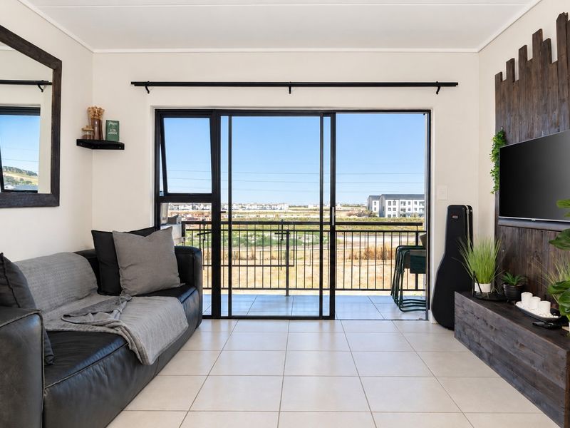 A bright living room featuring tiled flooring and large sliding glass doors that open onto a balcony with scenic views.