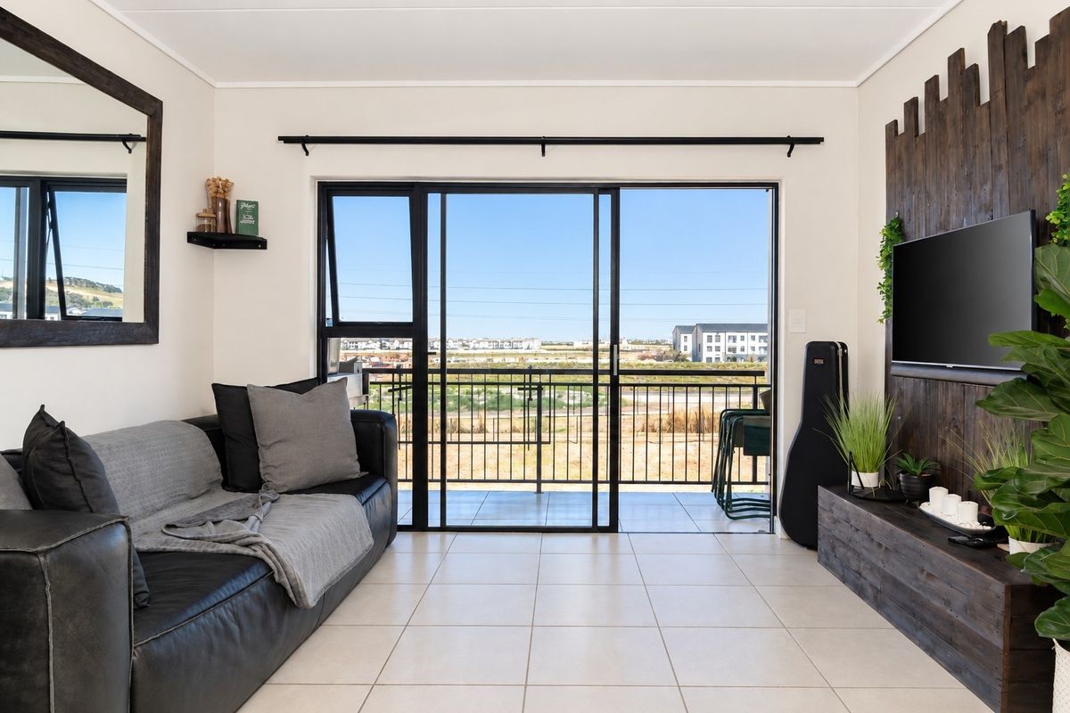 A bright living room featuring tiled flooring and large sliding glass doors that open onto a balcony with scenic views.