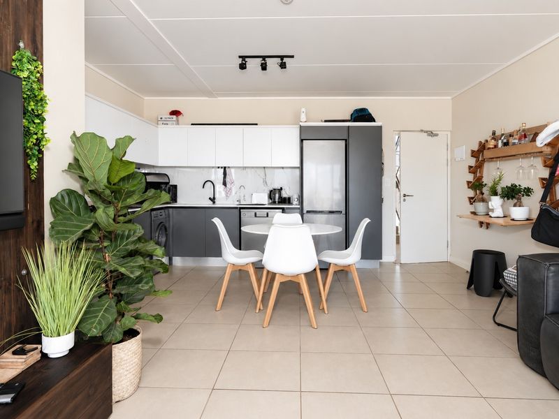 Modern open-plan living area featuring a sleek kitchen with white and grey cabinetry, marble-look backsplash, and neutral tiled flooring throughout.