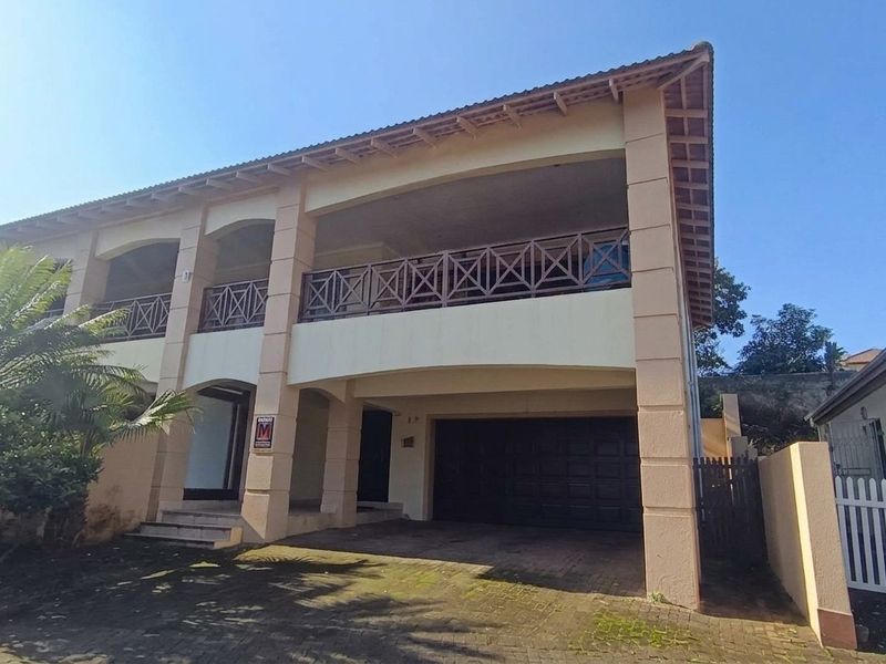Front elevation of a two-story townhouse featuring a paved driveway, double garage, and a spacious upper-level balcony with wooden balustrades.