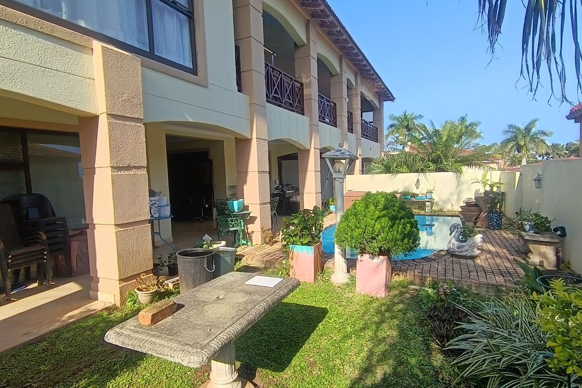 Rear exterior view of a townhouse featuring a swimming pool, paved patio area, and covered balcony with structural pillars.