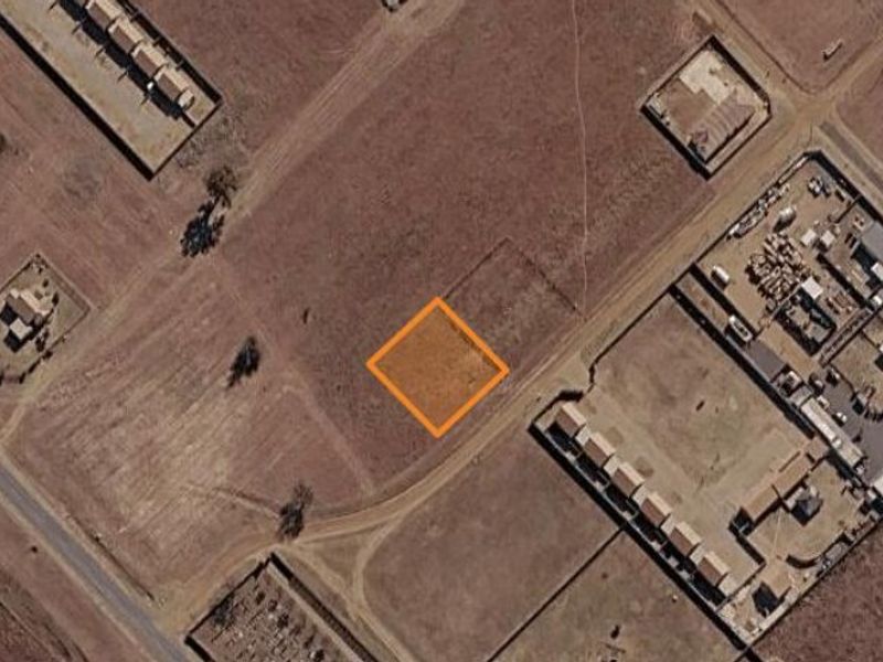 An aerial view of a vacant residential land plot highlighted with an orange border, situated in a developing area.