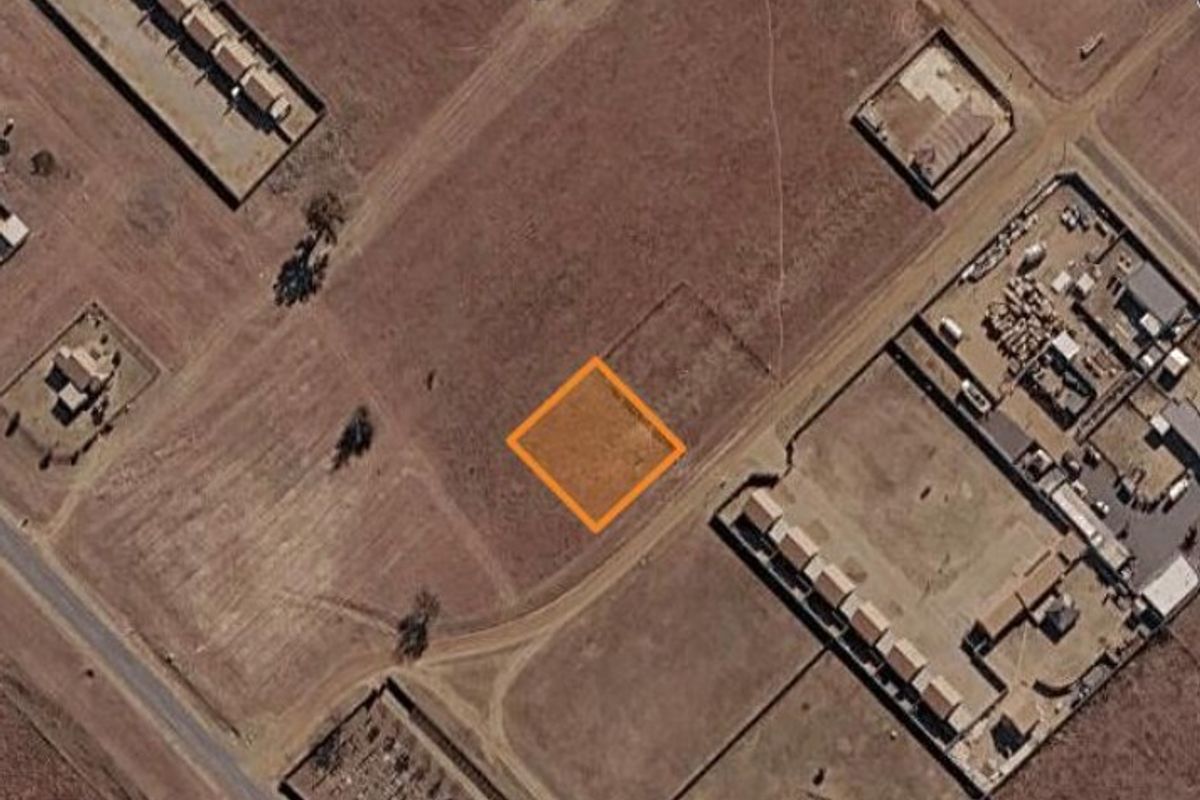 An aerial view of a vacant residential land plot highlighted with an orange border, situated in a developing area.