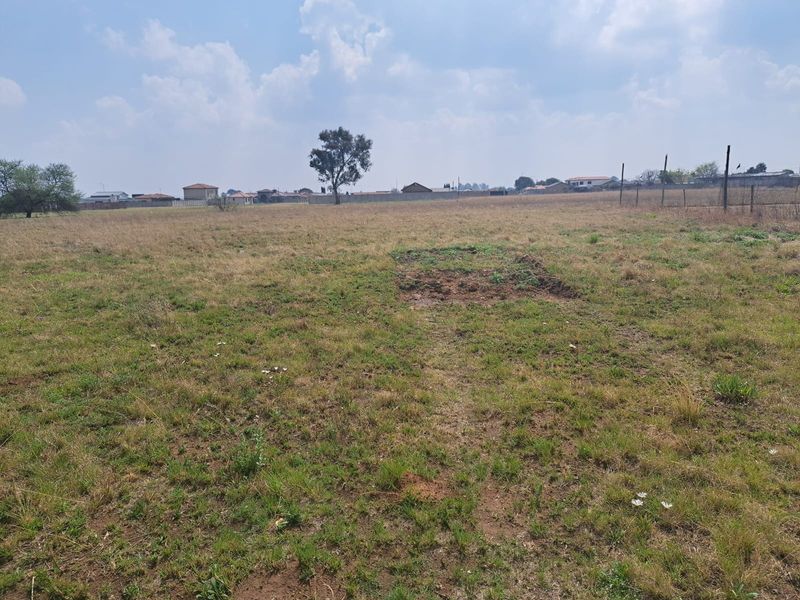 A wide-angle view of a vacant residential plot featuring open grass terrain and perimeter fencing, suitable for future development.