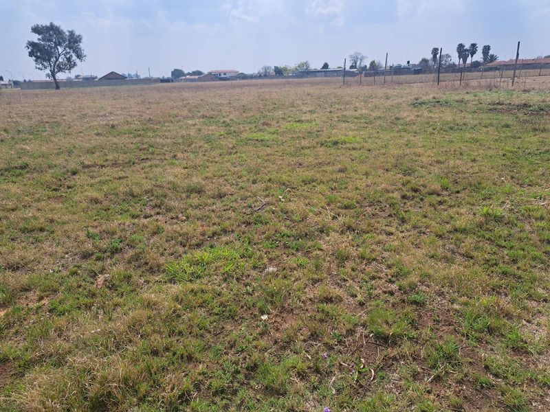 A wide, open vacant residential plot featuring natural grass coverage and perimeter wire fencing, suitable for future development.