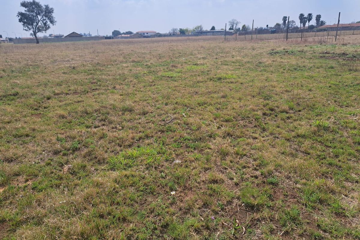 A wide, open vacant residential plot featuring natural grass coverage and perimeter wire fencing, suitable for future development.