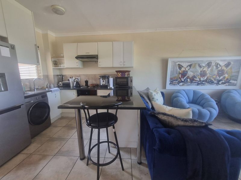 Open-plan kitchen and living area featuring tiled flooring, granite countertops, built-in cabinetry, and an integrated breakfast bar.