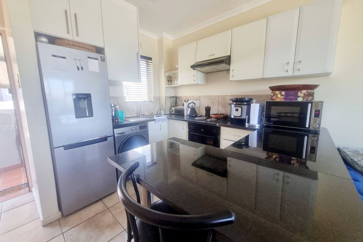 A functional kitchen featuring white cabinetry, dark granite countertops, a breakfast bar, and integrated appliances, finished with tiled flooring.