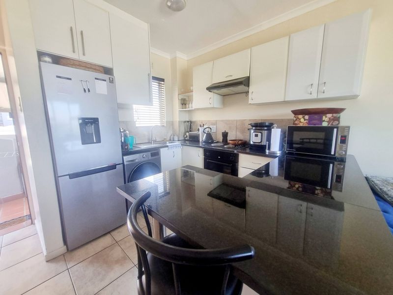 A functional kitchen featuring white cabinetry, dark granite countertops, a breakfast bar, and integrated appliances, finished with tiled flooring.