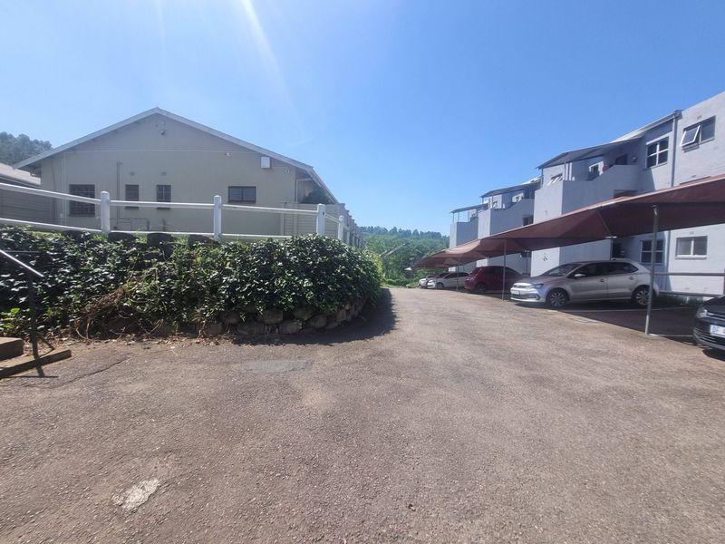Exterior view of the apartment complex driveway featuring covered parking bays, a retaining wall, and a white picket fence.