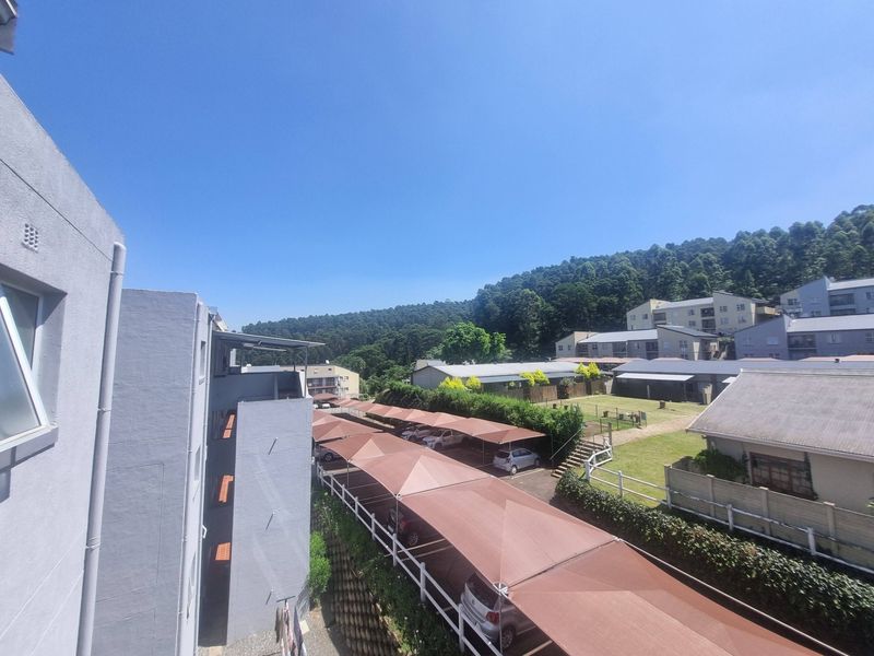 An elevated view of the apartment complex grounds, featuring covered parking structures, well-maintained lawns, and surrounding hillside scenery.
