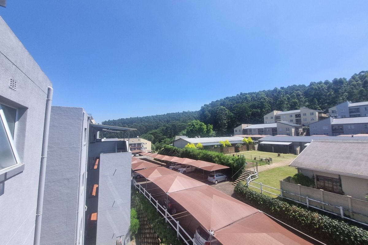 An elevated view of the apartment complex grounds, featuring covered parking structures, well-maintained lawns, and surrounding hillside scenery.