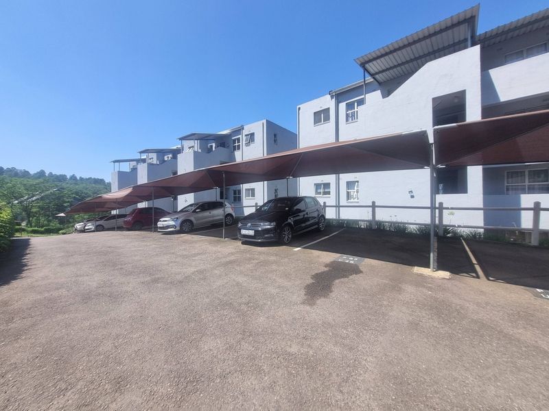 Exterior view of the apartment complex featuring a paved parking area with dedicated shade cloth carports for residents.