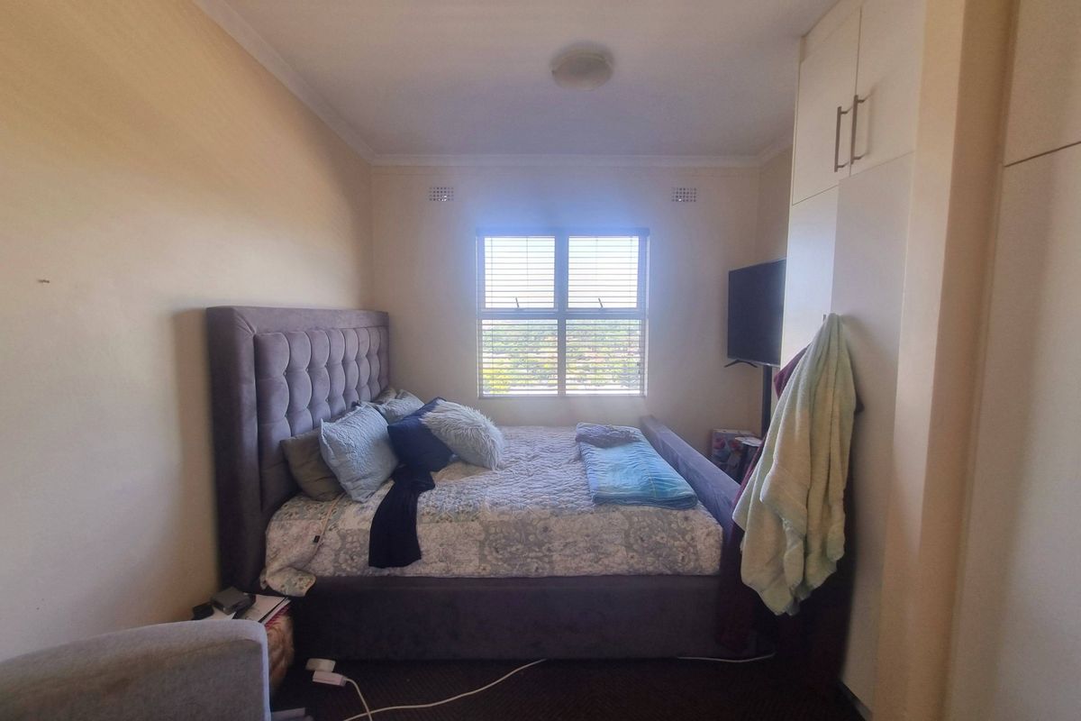 A functional bedroom featuring built-in cupboards, venetian blinds, and neutral wall finishes, offering a comfortable and practical living space.