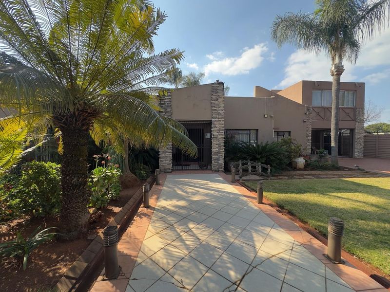 Front entrance view featuring a paved walkway, stone-clad facade, and established garden with mature palm trees and exterior lighting.