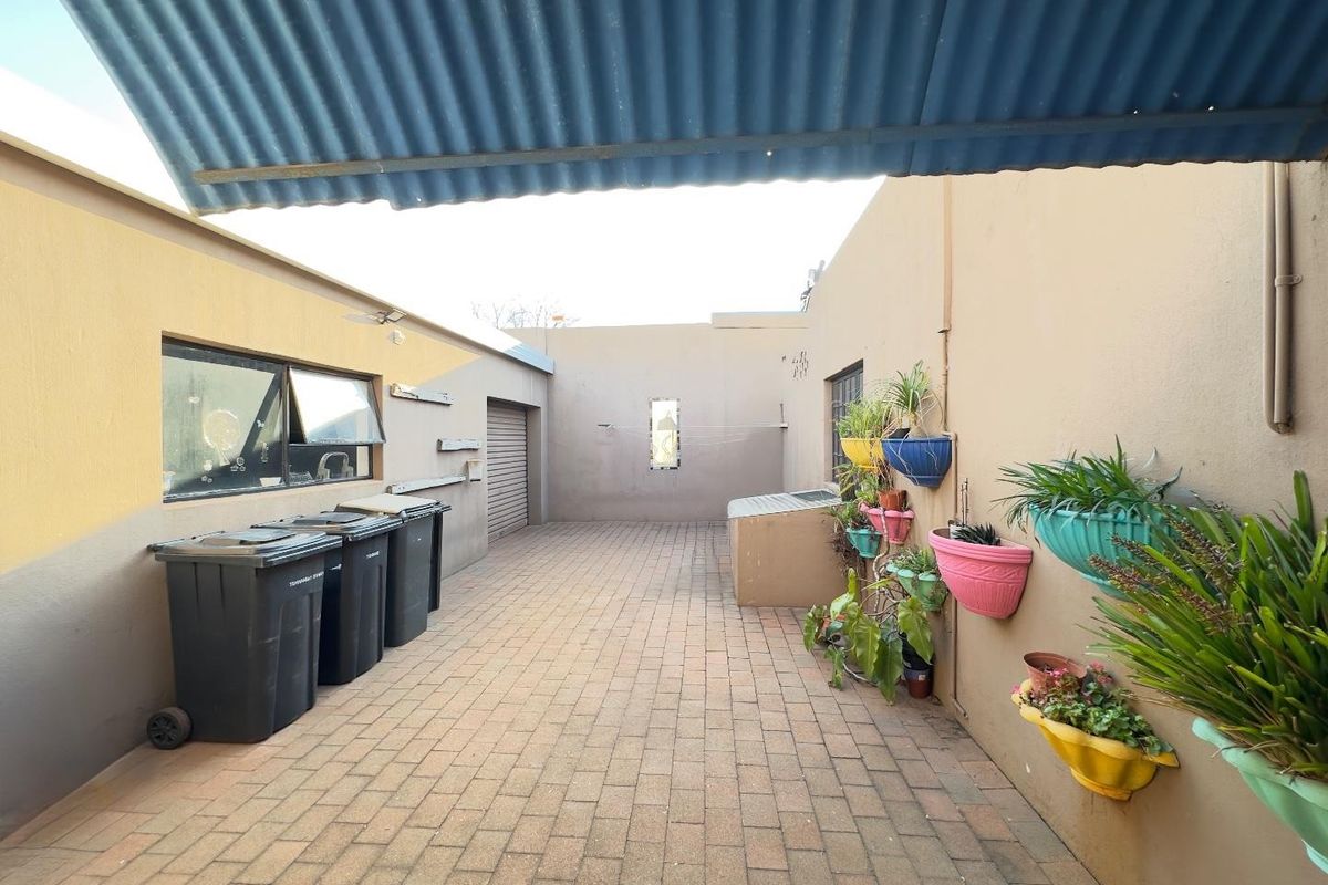 A paved rear courtyard area featuring a covered section, external access to the garage, and painted masonry walls.