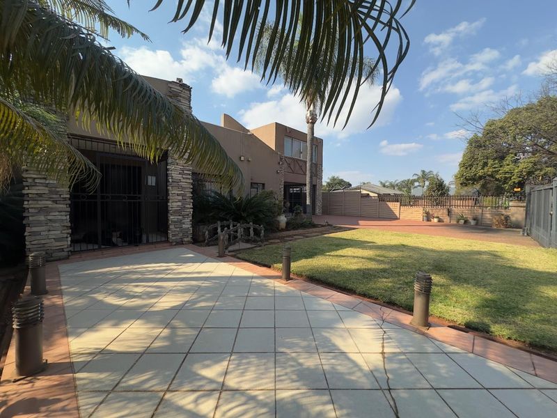 Front exterior view featuring a paved patio area, manicured lawn, stone-clad facade details, and secure perimeter fencing.