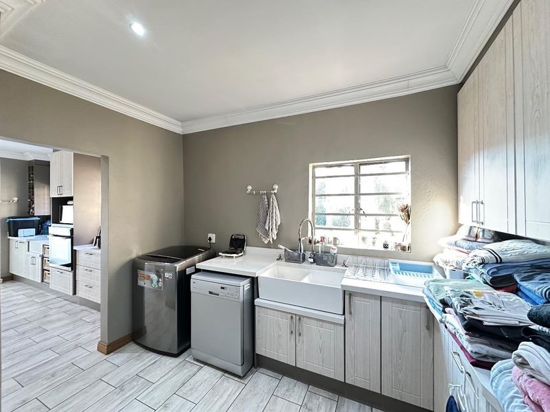 A functional laundry room featuring a farmhouse sink, built-in cabinetry, and tiled flooring, with an adjacent view into the kitchen area.