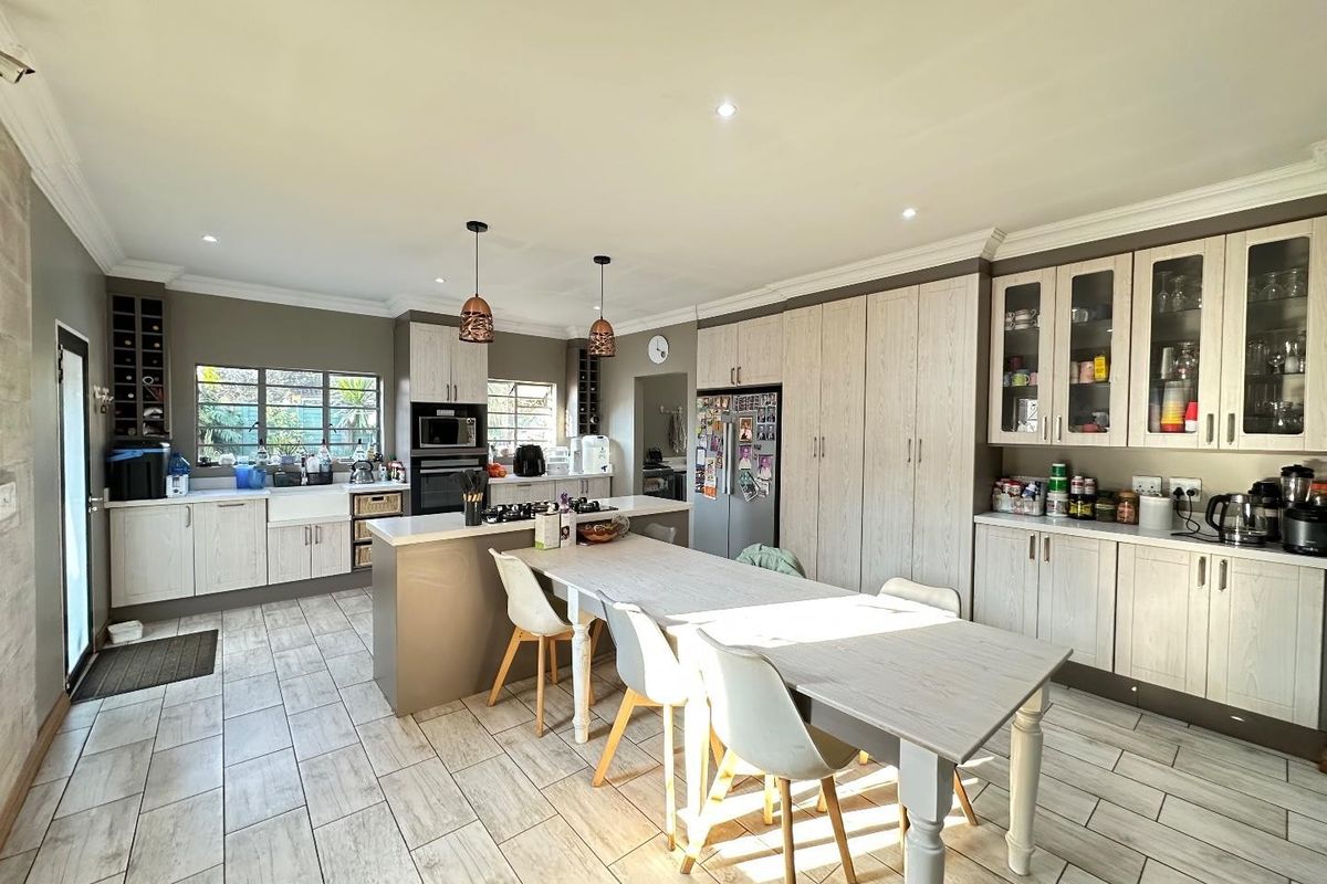 Spacious modern kitchen featuring light wood cabinetry, a central island with a gas hob, farmhouse sink, and integrated storage, finished with tiled flooring.
