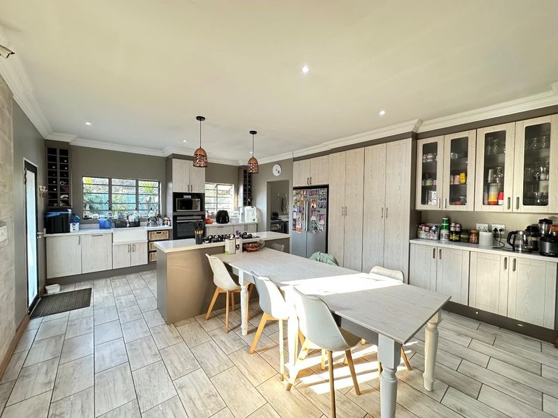 Spacious modern kitchen featuring light wood cabinetry, a central island with a gas hob, farmhouse sink, and integrated storage, finished with tiled flooring.