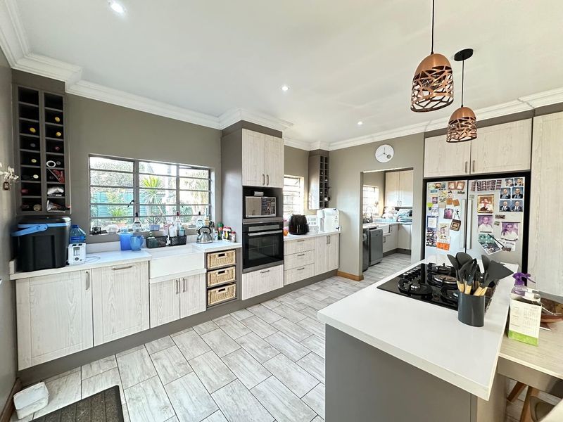 Modern kitchen featuring a central island with gas hob, farmhouse sink, built-in oven, wine storage, and neutral cabinetry with tiled flooring.