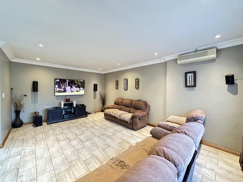 Spacious living room featuring tiled flooring, recessed downlighting, crown molding, and a wall-mounted split-system air conditioning unit.