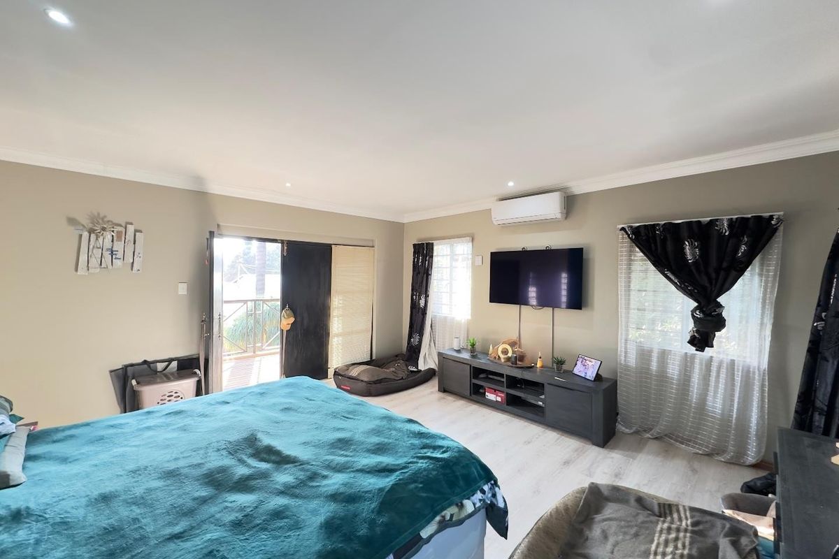 Spacious bedroom featuring laminate flooring, recessed downlighting, a split-system air conditioner, and direct access to an outdoor balcony through a sliding glass door.