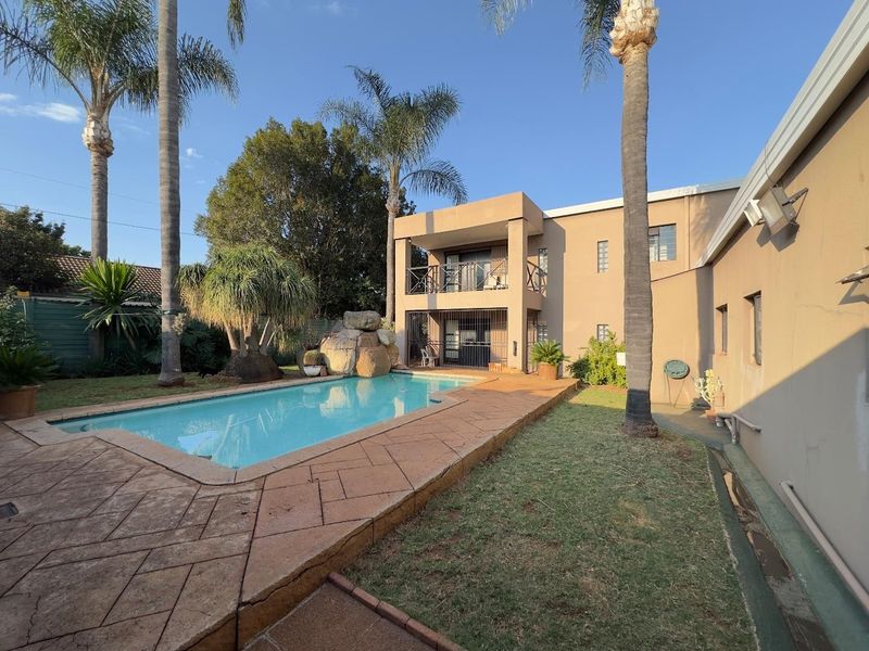 Rear exterior view featuring a swimming pool, paved deck, rock water feature, and a two-story building facade with a balcony.