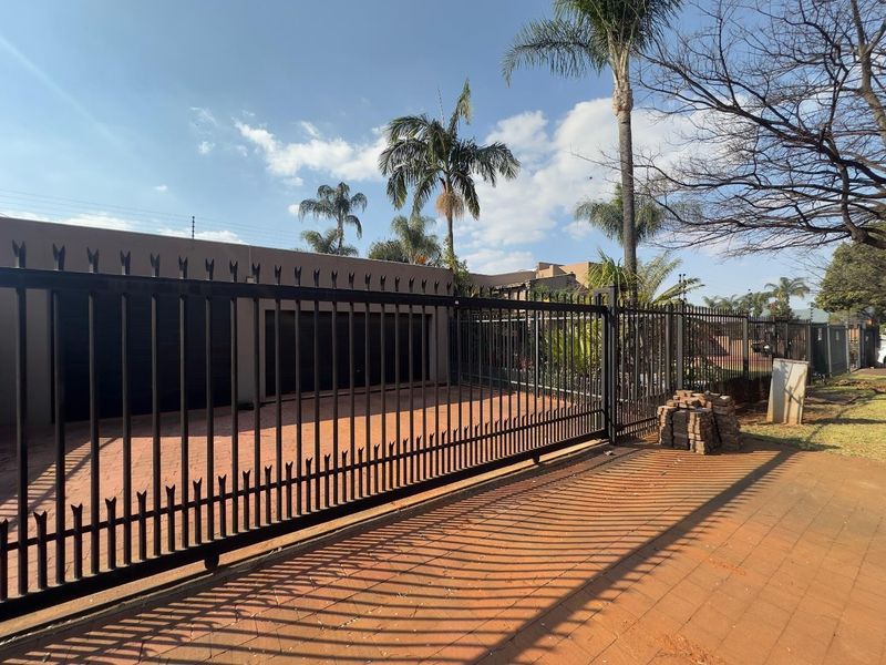 Front exterior view featuring a secure metal gate, paved driveway, and garage access with perimeter electric fencing.