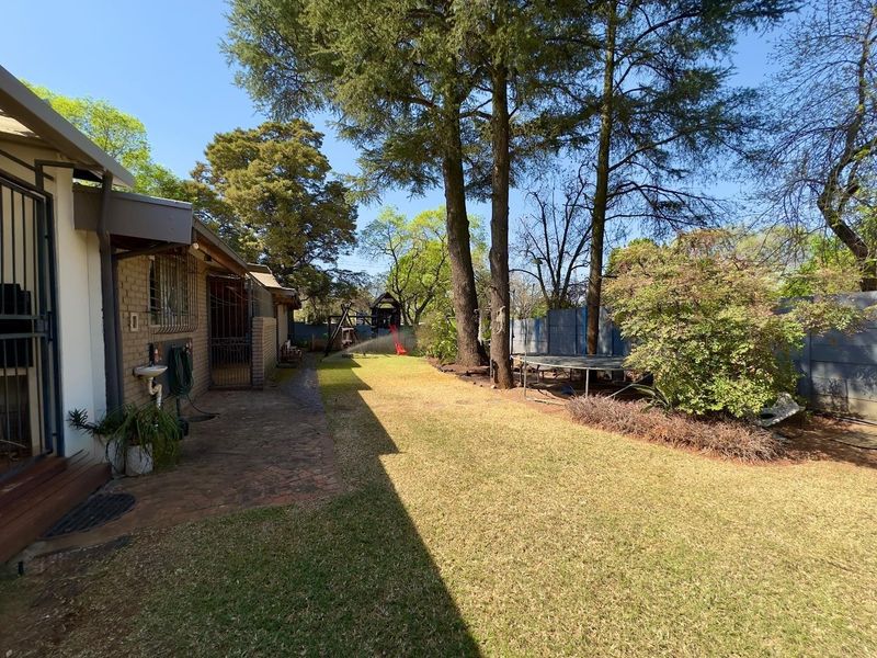 A spacious rear garden featuring a paved patio area, established trees, and a well-maintained lawn, providing a private outdoor space.