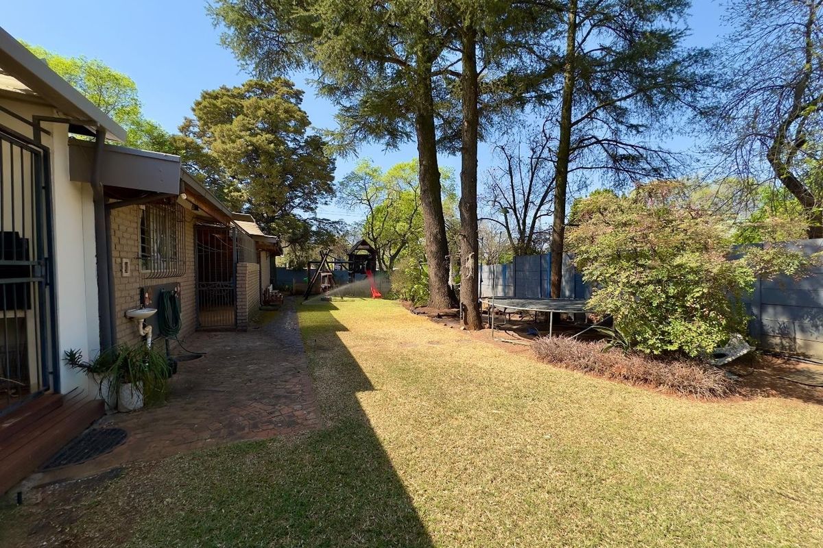 A spacious rear garden featuring a paved patio area, established trees, and a well-maintained lawn, providing a private outdoor space.