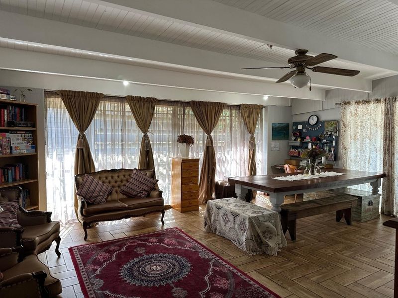 Spacious open-plan living and dining area featuring exposed beam ceilings, herringbone tile flooring, and large windows providing ample natural light.