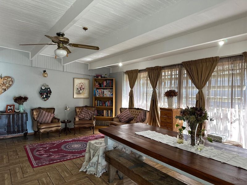 Spacious open-plan living and dining area featuring exposed beam ceilings, parquet flooring, and large windows that provide ample natural light.